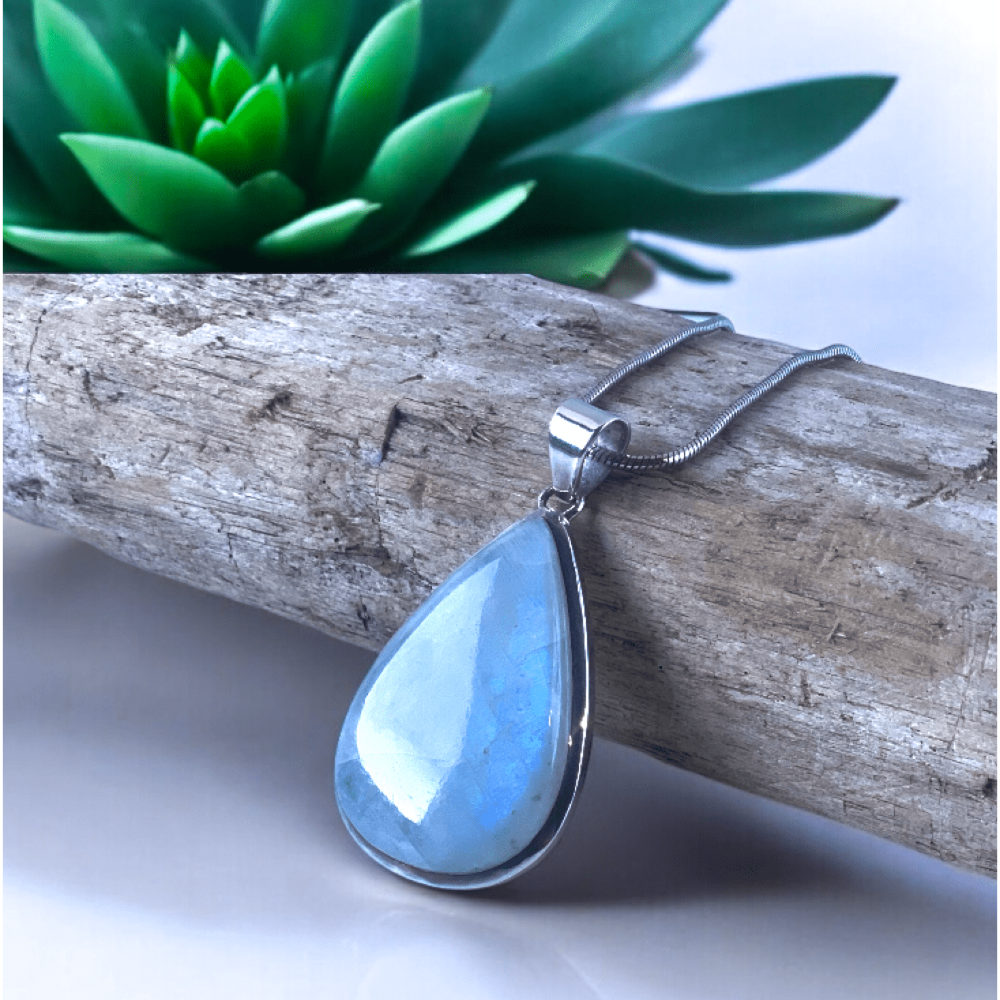 Pendentif pierre de lune posé sur bois flotté entouré de succulents